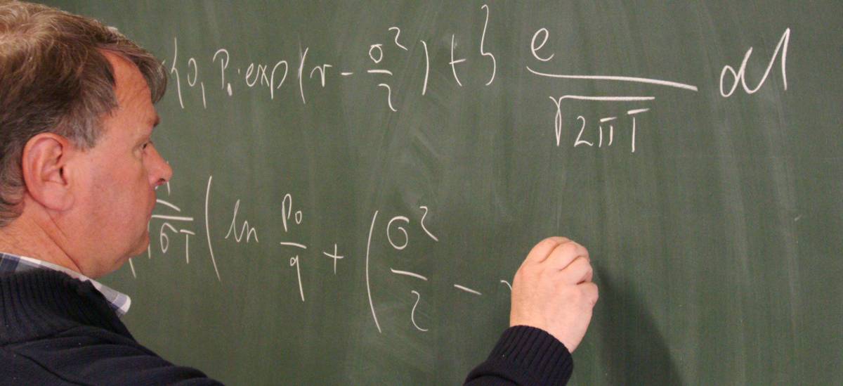 Mann schreibt mathematische Formeln an eine Tafel im Seminarraum