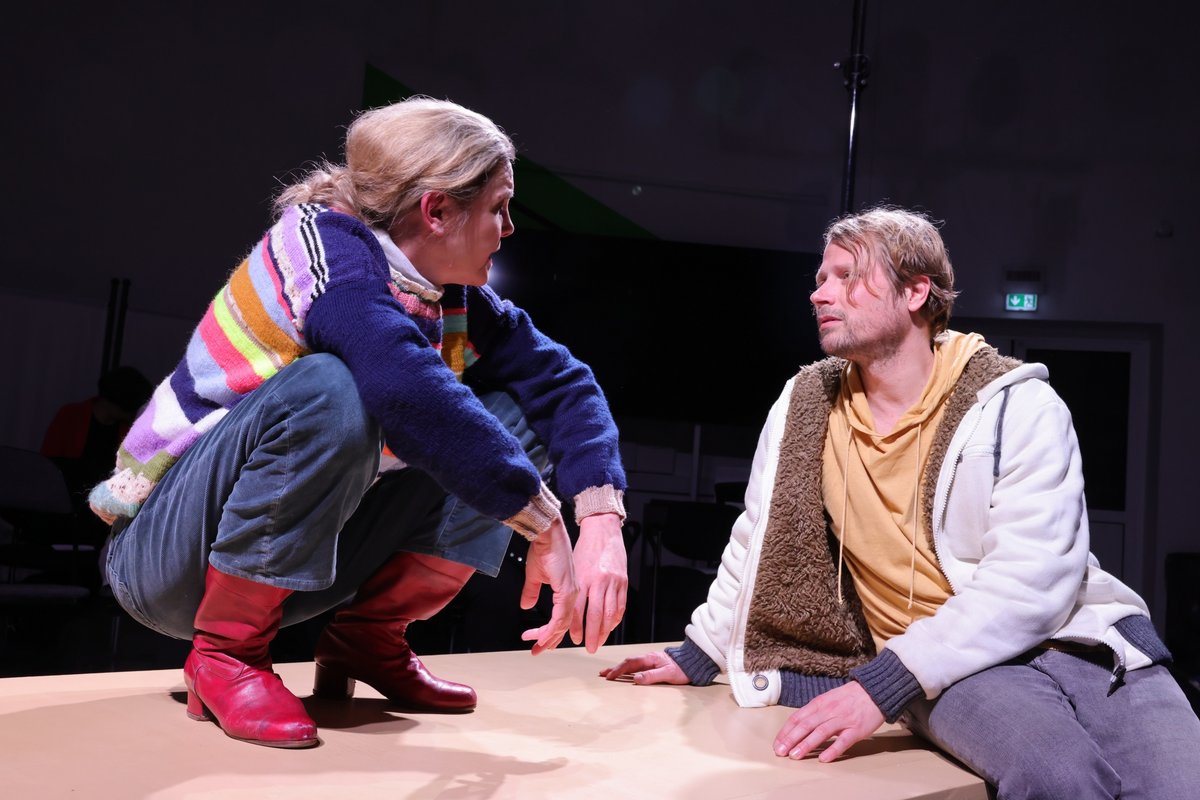An actress and an actor are talking while squatting on the stage.