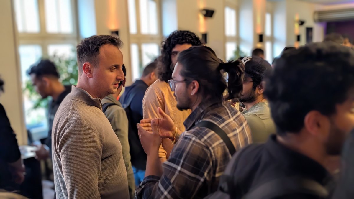 Zwei Männer unterhalten sich umgeben von weiteren Personen.