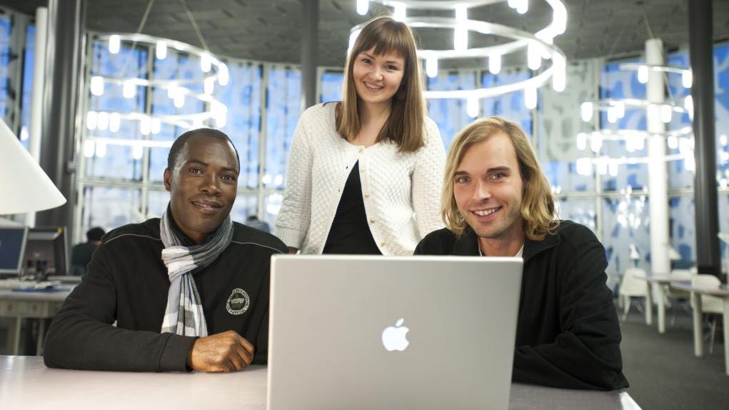 Drei junge Menschen sitzen an einem Laptop