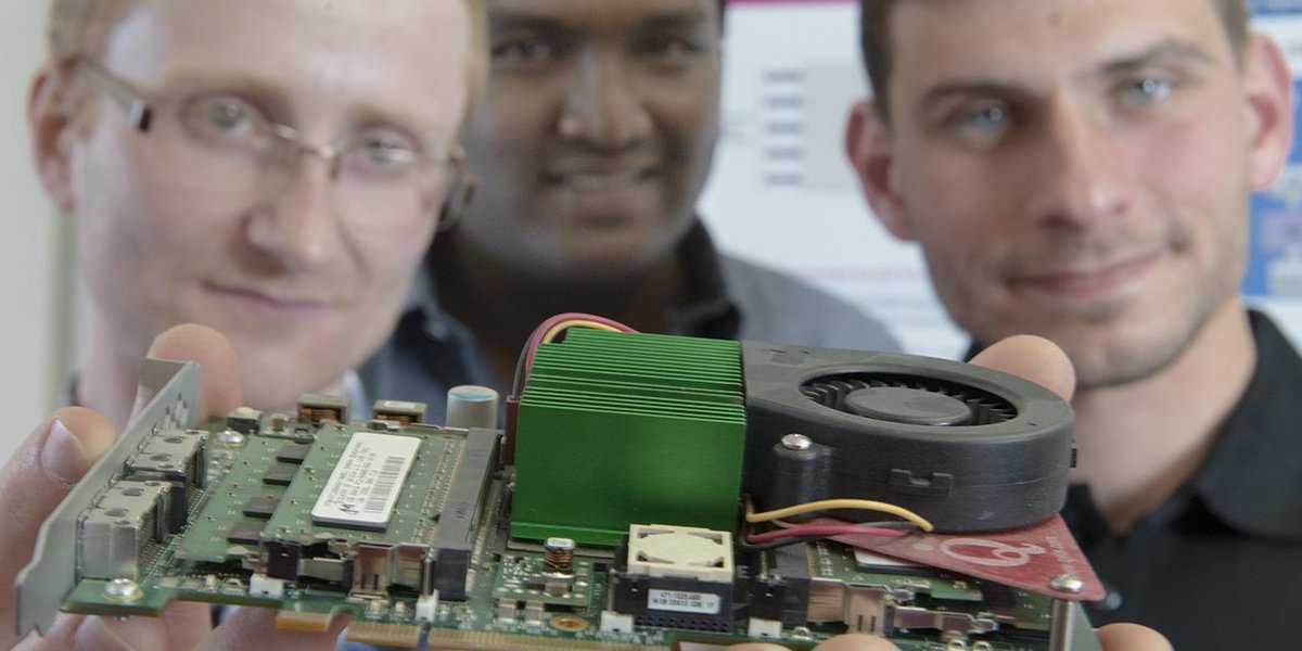 Three PhD students holding a graphics card in front of the camera