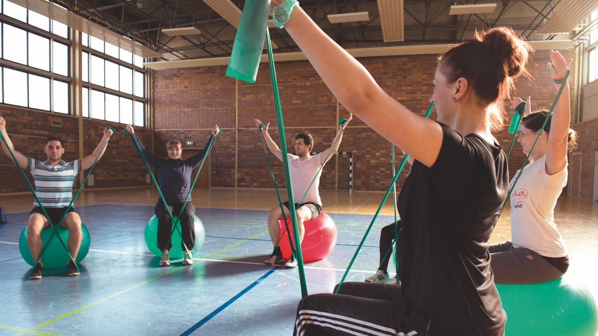 Studierende der Therapiewissenschaften machen Übungen mit Terrabändern und Gymnastikbällen in der Turnhalle am Campus Senftenberg