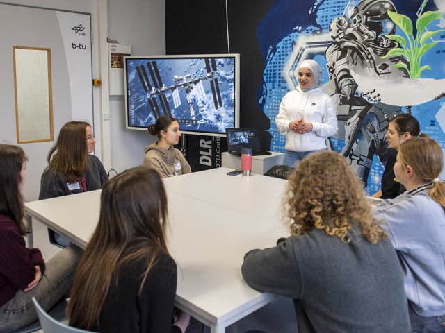 Schoolgirls, sitting at a table, follow a lecture.