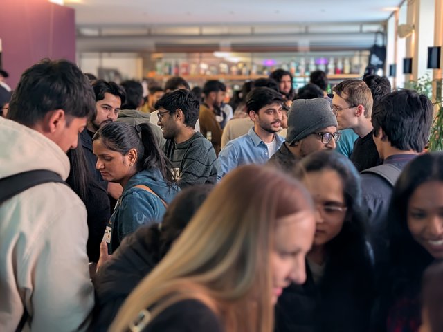 Viele Perosnen stehen ineiner Bar und unterhalten sich angeregt. 