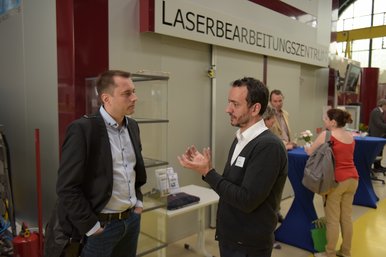 Zwei Teilnehmer des BTUTransferTages sind im Gespräch und stehen dabei in der Panta Rhei Halle vor dem Laserbearbeitungszentrum.