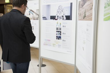 Ein Teilnehmer des BTUTransferTages steht vor einer Wand und schaut sich die Posterpräsentationen an. 