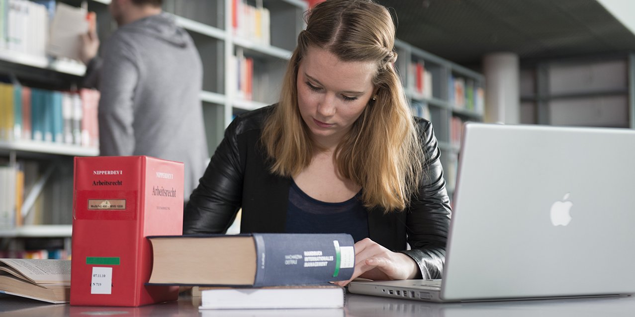 Studentin im Studiengang Wirtschaftsrecht für Technologieunternehmen welzt Gesetzestexte in der Bibliothek