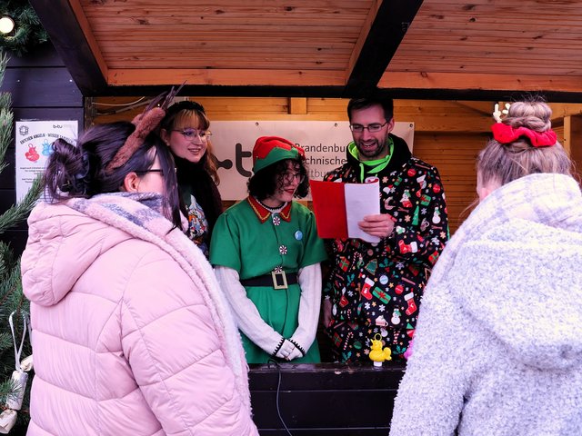 Students in a Christmas hut talk to visitors. 