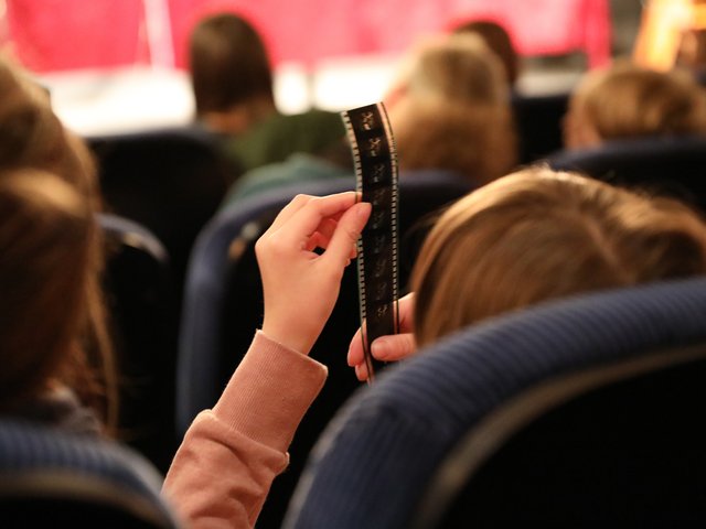 Kinder sitzen im Kinosaal. Nahaufnahme Kind von hinten, dass sich einen Negativstreifen anschaut