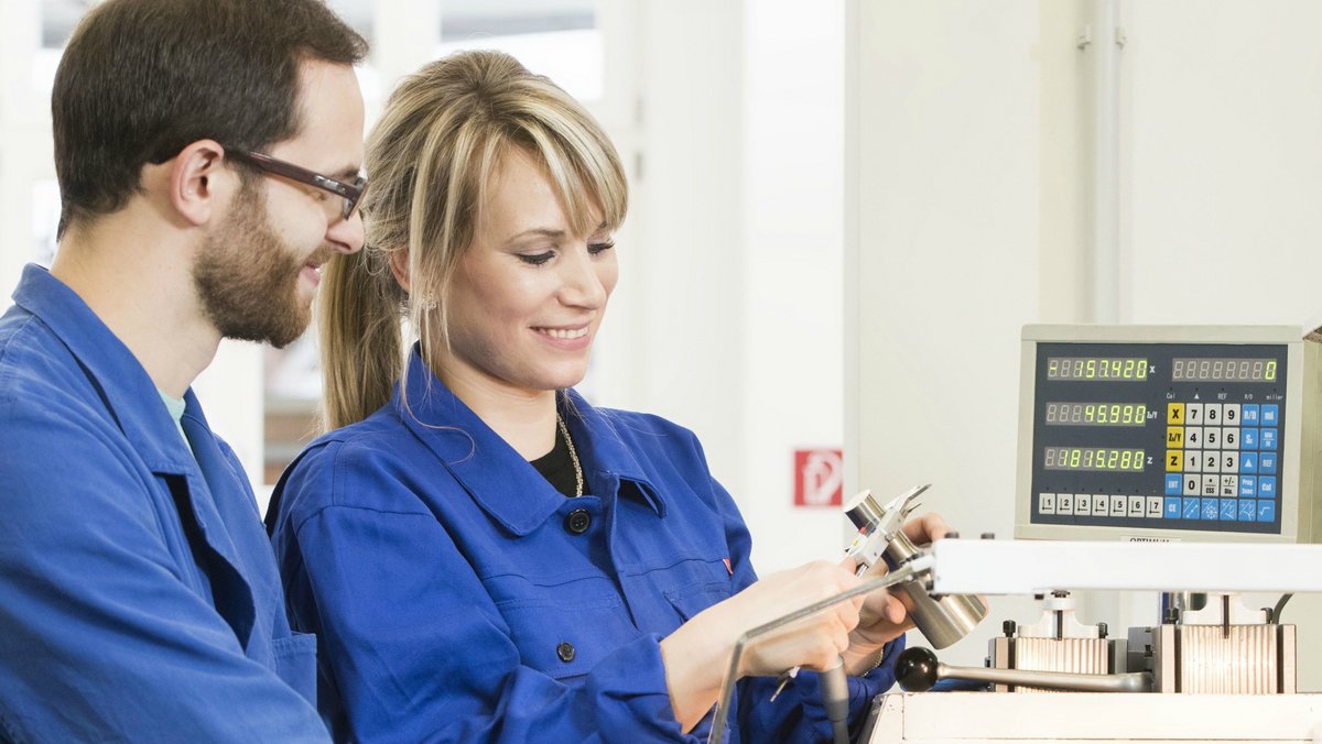 Zwei Studierende wenden ihr erlerntes Fachwissen praktisch an einer Fräsmaschine an. Mithilfe einer Schiebelehre wird die Maßhaltigkeit des hergestellten Zylinders gemessen.