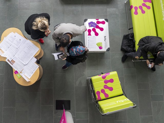 Das Foto zeigt den InfoPoint von oben. Zu sehen sind ein kleiner Tisch, zwei Sitzbänke und drei junge Menschen.