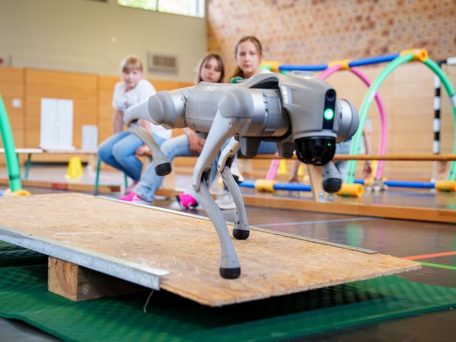 A dog robot is controlled by schoolgirls using a seesaw.
