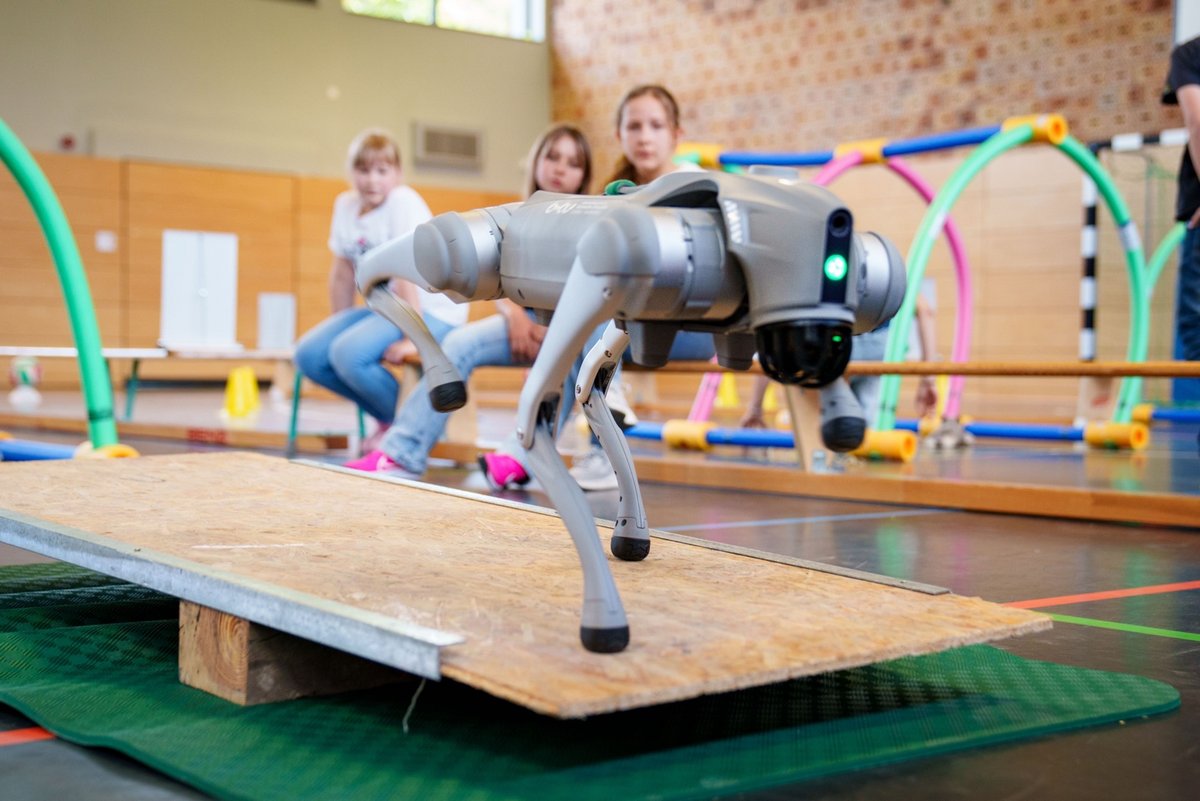A dog robot is controlled by schoolgirls using a seesaw.