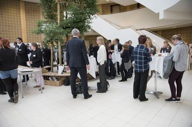 Teilnehmerinnen und Teilnehmer stehen in Grüppchen, teils an Stehtischen, im Eingangsbereich des Konrad-Zuse-Medienzentrums.