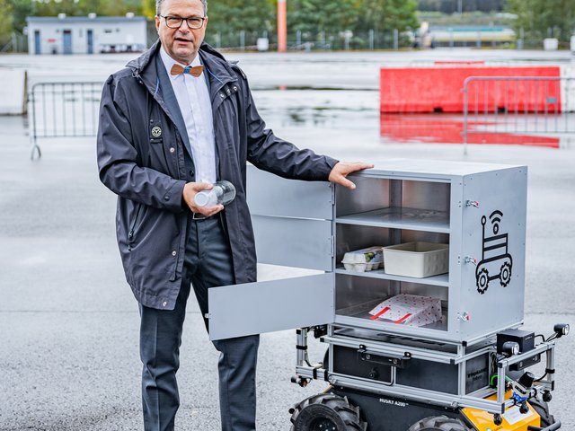 Prof. Dr.-Ing. Sylvio Simon steht neben einem Lieferroboter. 