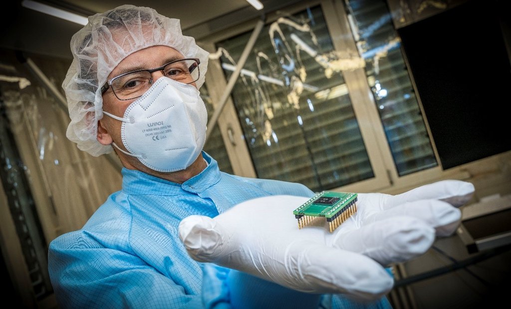 Prof. Dr. Harald Schenk im Labor mit Schutzkleidung und einem Microchip in der Hand