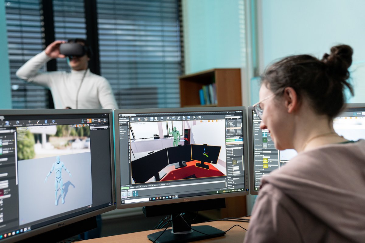 A student edits graphics on a PC, with a student wearing VR goggles in the background. Photo: BTU, Sebastian Rau