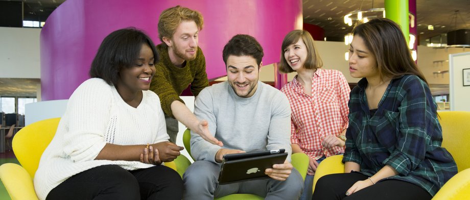 Fünf internationale Studierende, teils sitzend, teils stehen, schauen im Foyer des IKMZ in Cottbus gemeinsam auf ein Tablett.