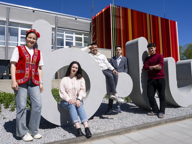 Vier Studierende an dem fast zwei Meter hohen plastischen Schriftzug b-tu.gübergroßen Logo der BTU