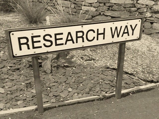 Das Bild zeigt eine Sepia-Fotografie eines Schilds mit der in Großbuchstaben abgebildeten Aufschrift „Research Way“.