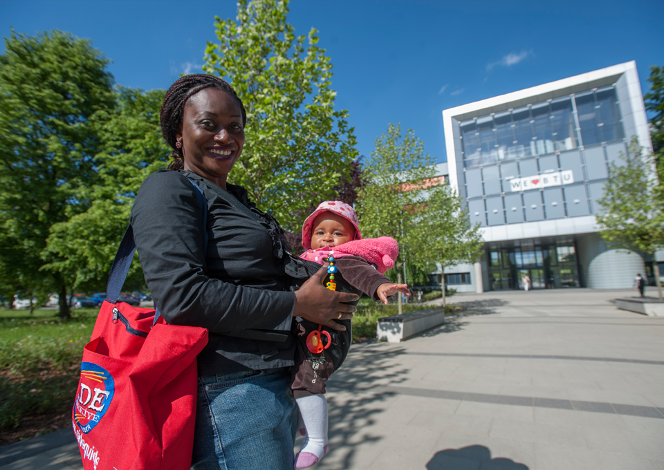 Das Bild für den Grund 3: Chancengleichheit - Auf dem Bild steht eine Studentin mit ihrem Kind vor dem Hauptgebäude der BTU