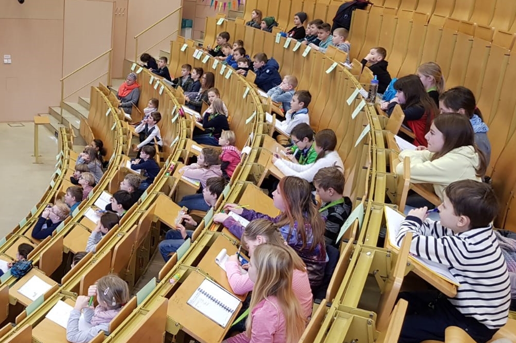 Mädchen und Jungen sitzen im Hörsaal und folgen einer Kinderuni-Vorlesung. Foto: Mark Nielsen