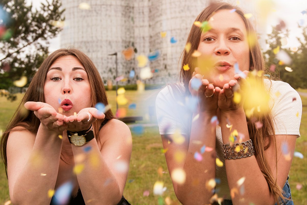 Zwei junge Frauen pusten Konfetti in die Kamera