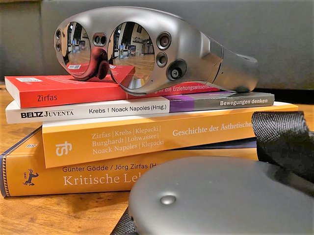 A stack of books and VR glasses symbolize the topic of digitization in social work.