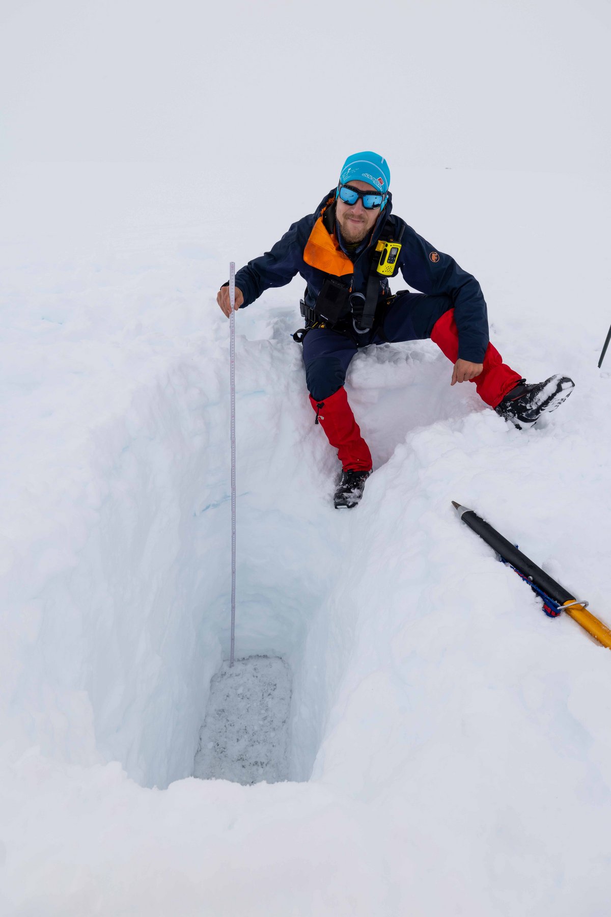 A scientist is sitting by the large hole in the ice, holding a plumb line