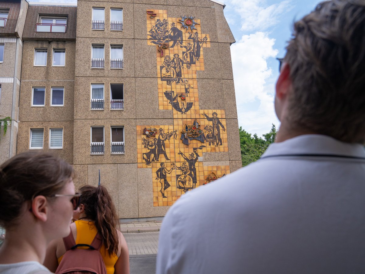Die Studierenden schauen sich ein sorbisches Mosaik an einer Häuserwand in der Innenstadt an.