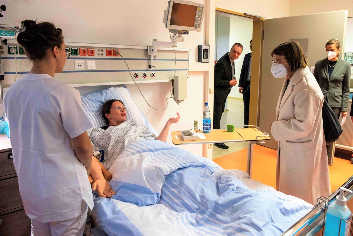 Ministerin Nonnemacher spricht im SkillsLab mit eiern Studentin und eine Mitarbeiterin, bei der Simulation ein Blutentnahme am Krankenbett. (Foto: BTU, Ralf Schuster)