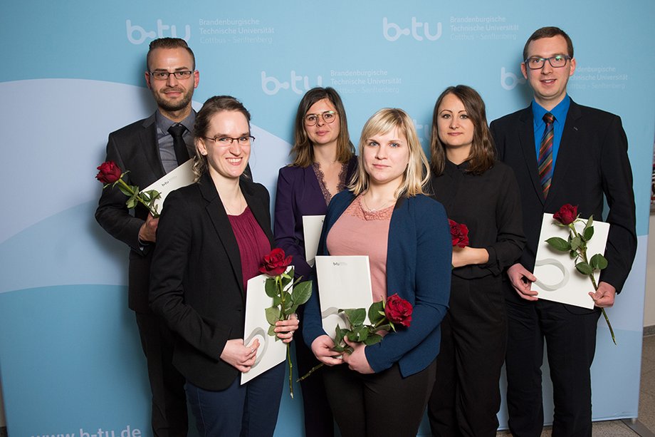Die Preisträger mit Urkunden und Blumen in der Hand vor der Fotowand
