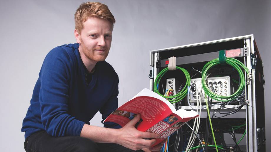 Ein Student liest ein Fachbuch während er vor einem Technik Rack sitzt