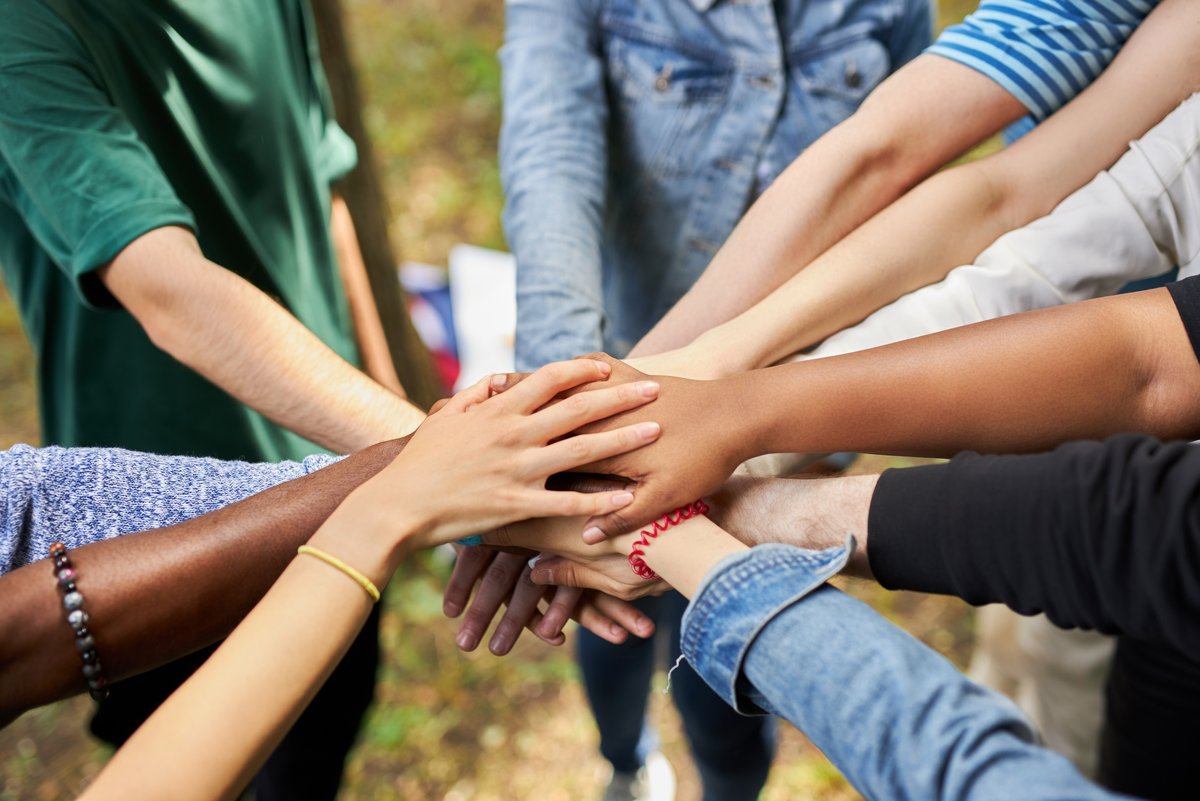 Diverse Menschen stehen im Kreis und halten ihre Hände in der Mitte übereinander zusammen, Quelle: Adobe Stock - 364510193