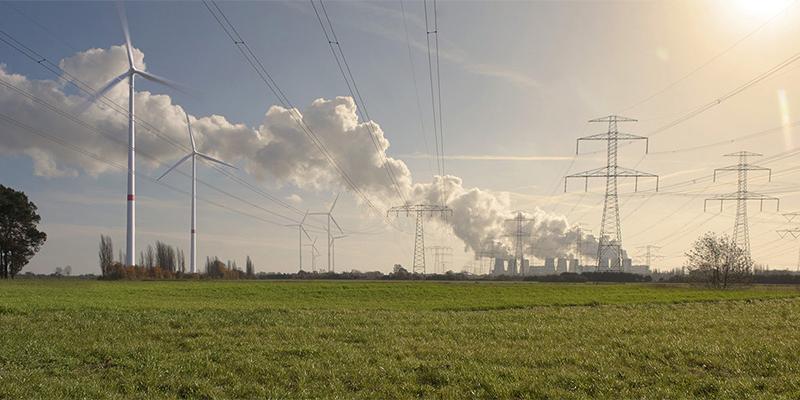 Grüne Wiese mit Stromtrassen, Windkraftanlagen und Kohlekraftwerk im Hintergrund