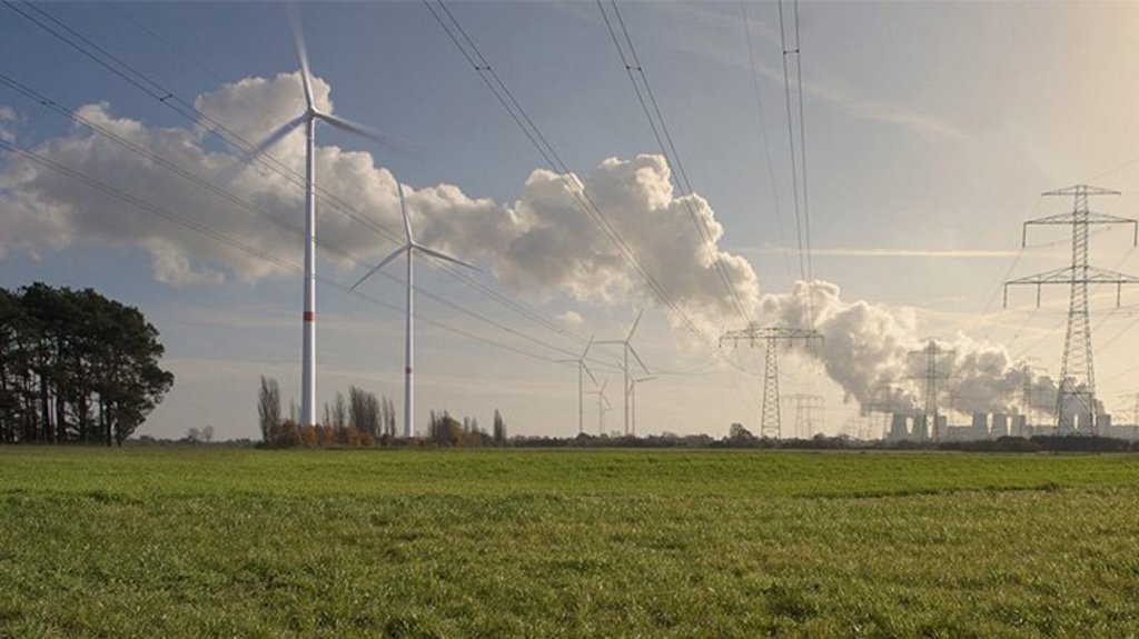 Grüne Wiese mit Stromtrassen, Windkraftanlagen und Kohlekraftwerk im Hintergrund