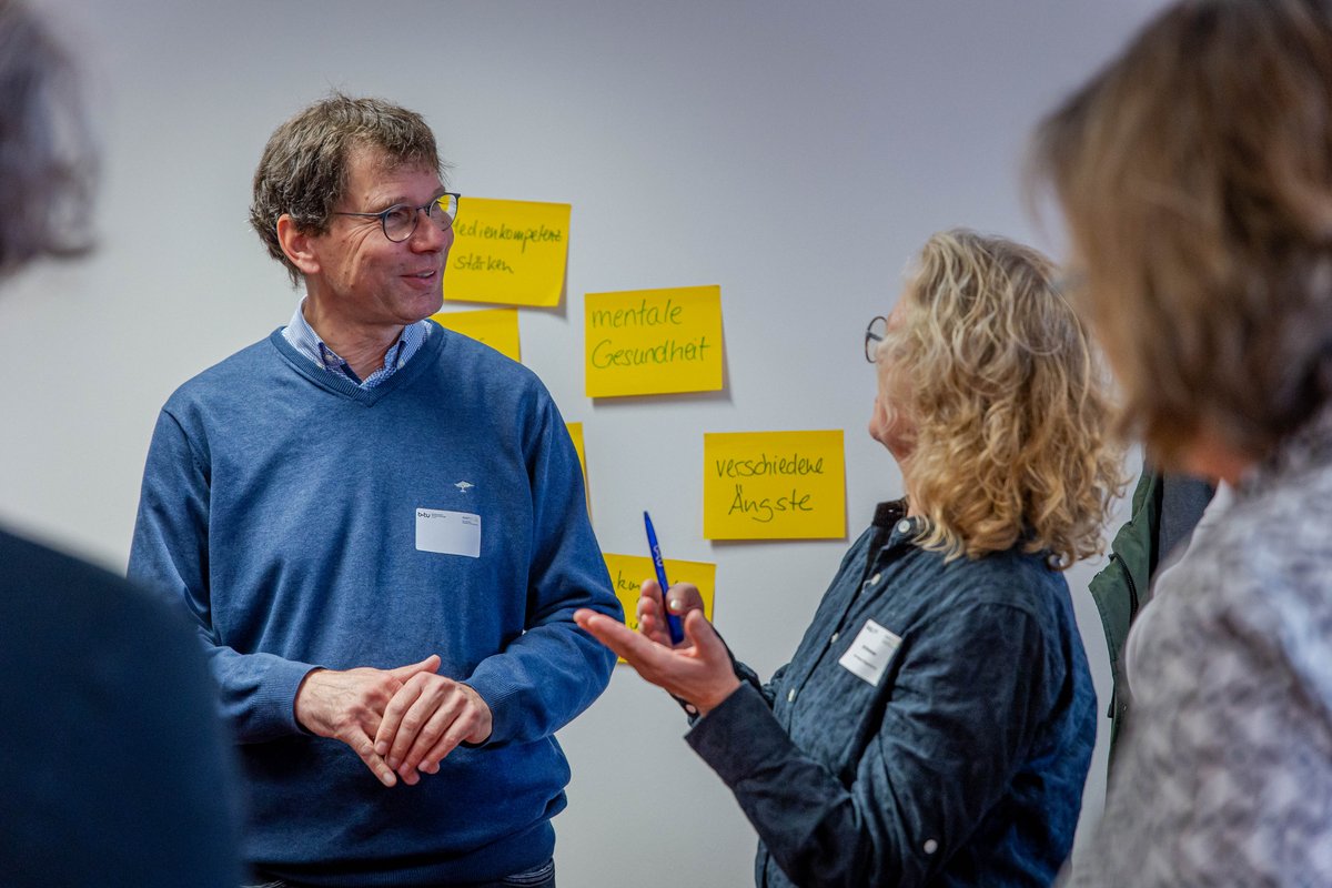 Teilnehmende der Tagung diskutieren stehend im Rahmen des Workshops zum Thema Gesundheit.