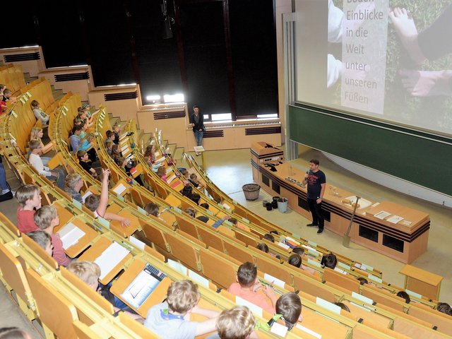 An der Kinderuni der BTU teilnehmende Mädchen und Jungen sitzen im Hörsaal und folgen einer Vorlesung.