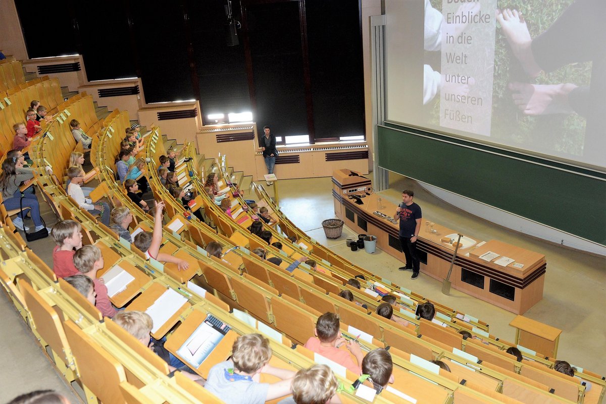 An der Kinderuni der BTU teilnehmende Mädchen und Jungen sitzen im Hörsaal und folgen einer Vorlesung.