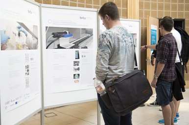 Zwei Teilnehmerinnen (Rücken dem Fotografen zugewandt) und ein Teilnehmer des BTUTransferTages betrachten gemeinsam eine Posterpräsentation.