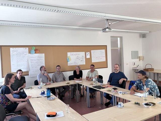 Das Foto zeigt Tische, die in enem Rechteck zusammengestellt sind und Teilnehmende des Workshops.