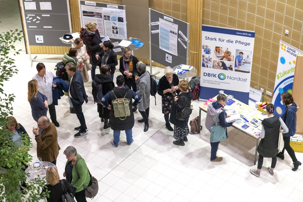Marktplatzbegegnungen „Rund um die Pflegewissenschaft“ im Foyer des Konrad-Zuse-Medienzentrums. Teilnehmende stehen in Gruppen zusammen un diskutieren.