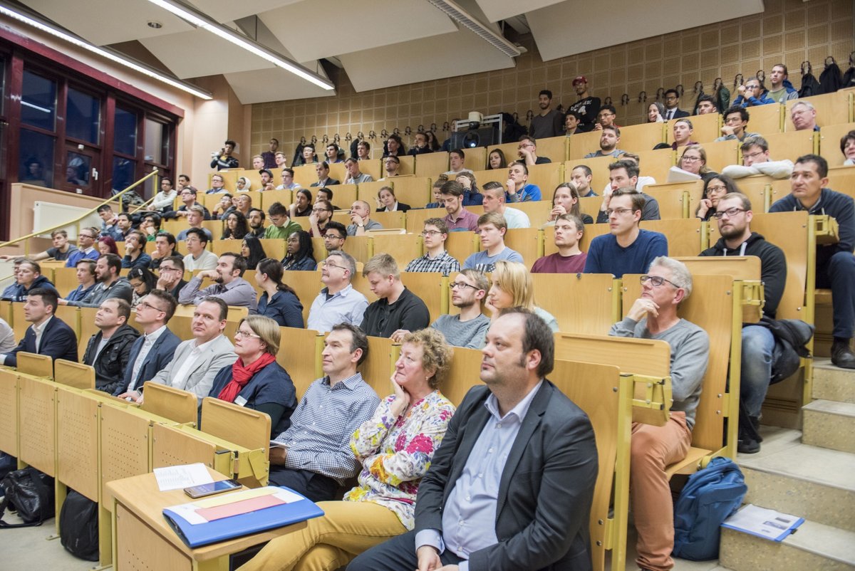 Studierende, Lehrende und Unternehmensvertreter im Hörsaal sitzend.