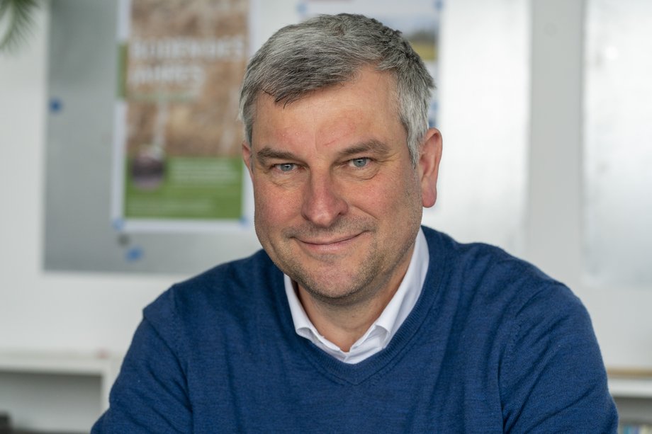 Professor Raab, the Dean of Faculty 2, is sitting in a bright room in front of a poster; he is wearing a blue jumper and is looking directly into the camera with a smile