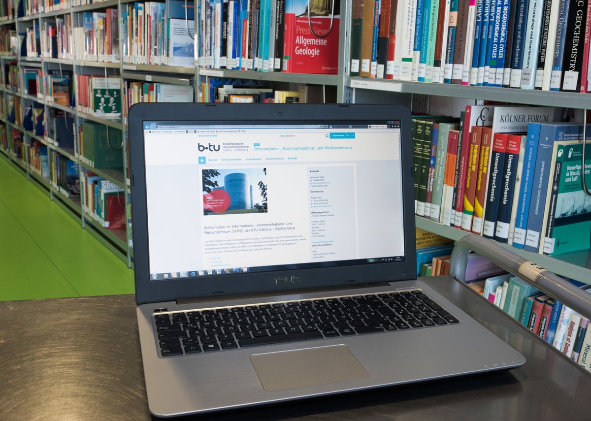 Ein Laptop steht vor einem Bücherregal in der Universitätsbibliothek.