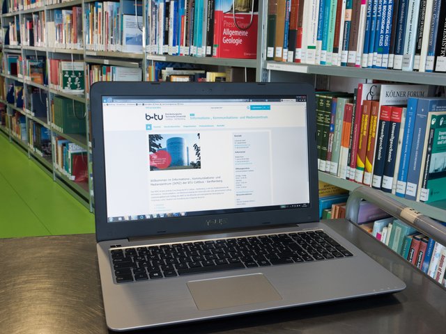 Ein Laptop steht vor einem Bücherregal in der Universitätsbibliothek.