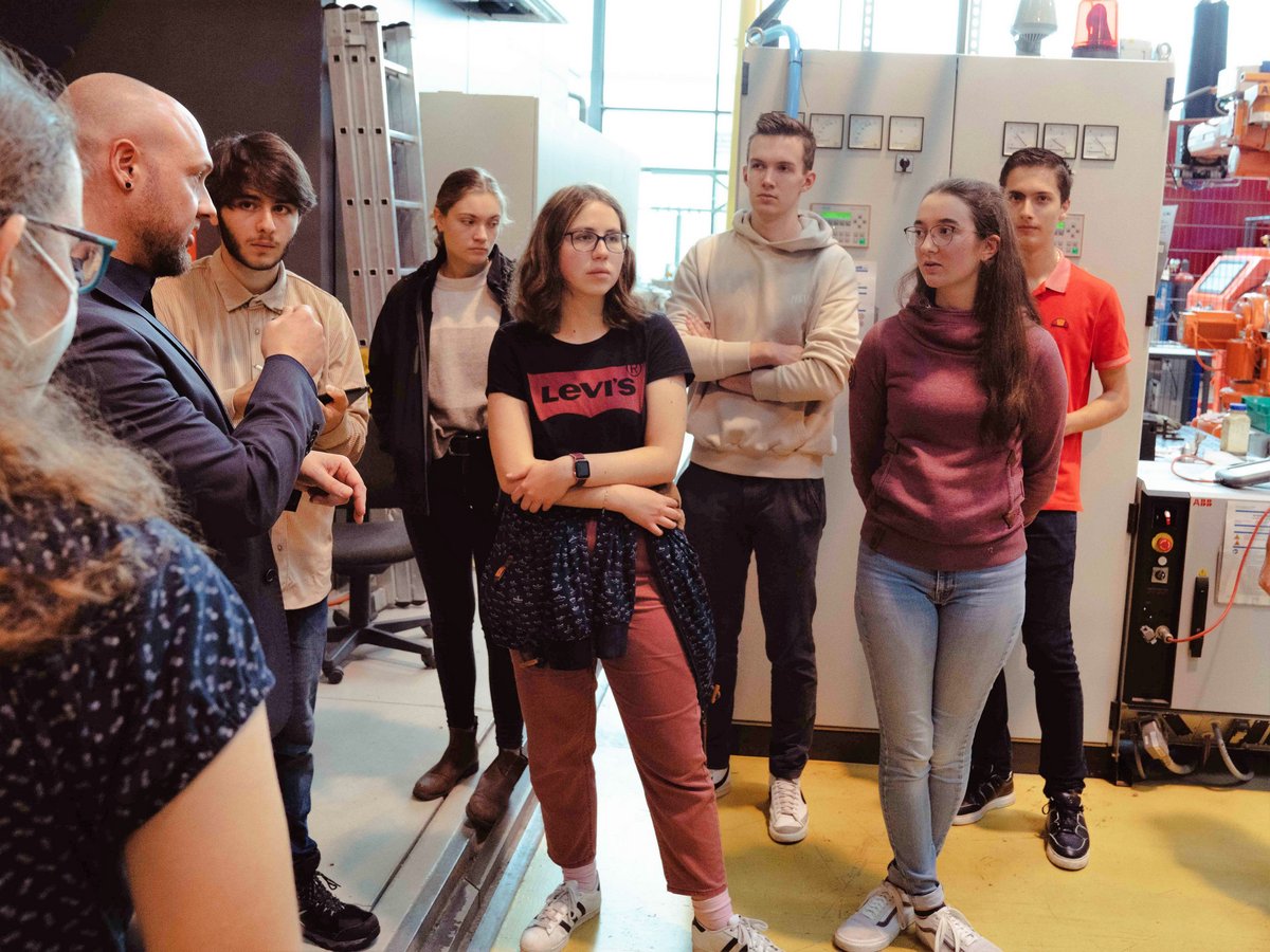 Young people, standing in a mechanical engineering laboratory, follow a scientist's explanations. Photo: BTU, Avishek Shovakar