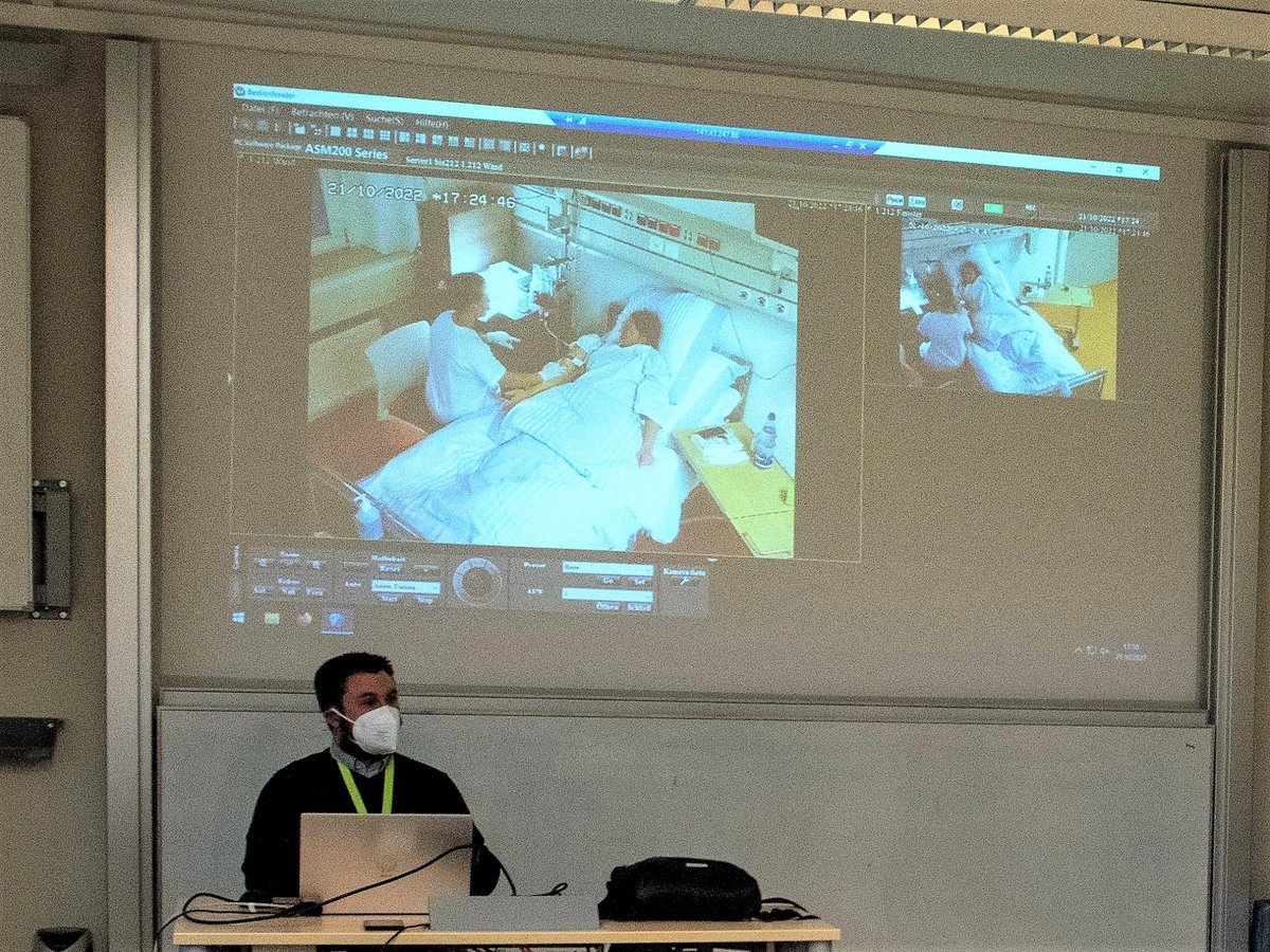 Videoaufnahmen aus einem Krankenzimmer (SkillsLab) werden an eine Tafel projiziert. Im Vordergrund sitzt ein Dozent. (Foto: BTU, Ralf Schuster) 