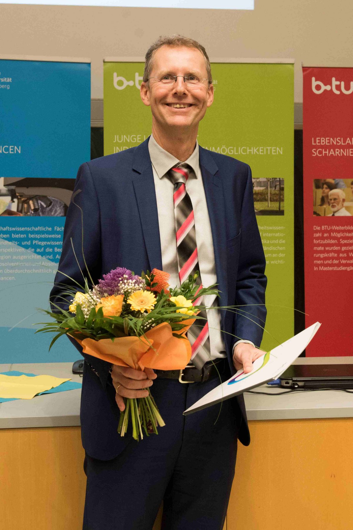 Honorarprofessor Dr. Michael Lehmann mit Urkunde un Blumenstrauß im Hörsaal stehend.