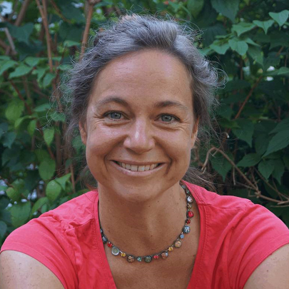 smiling woman photographed outdoors in front of a green hedge